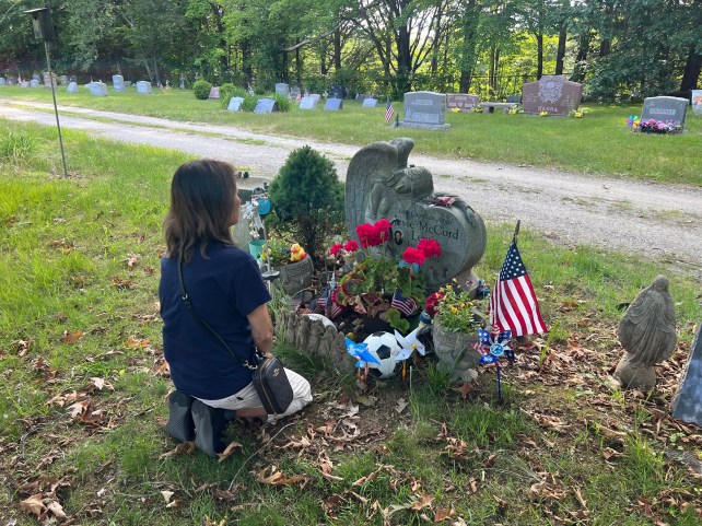 Woman kneeling on the ground in front of a grave.