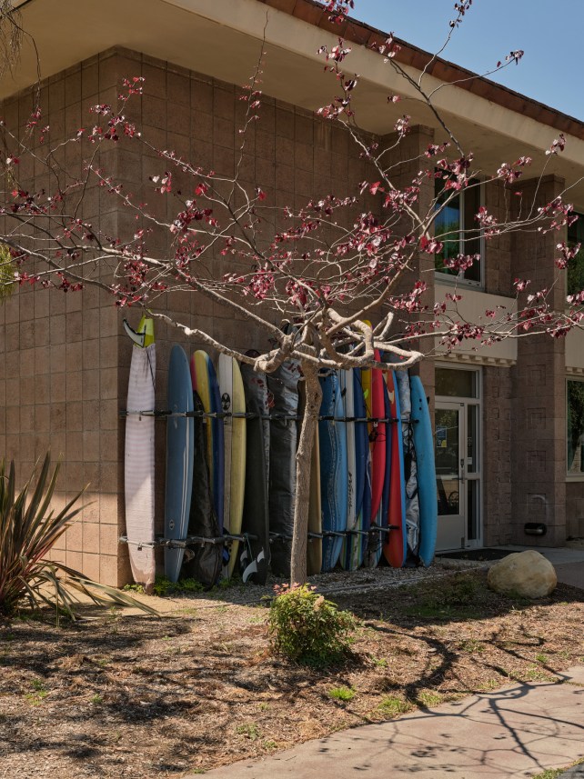 A line of surfboards sit in a rack next to a dorm.