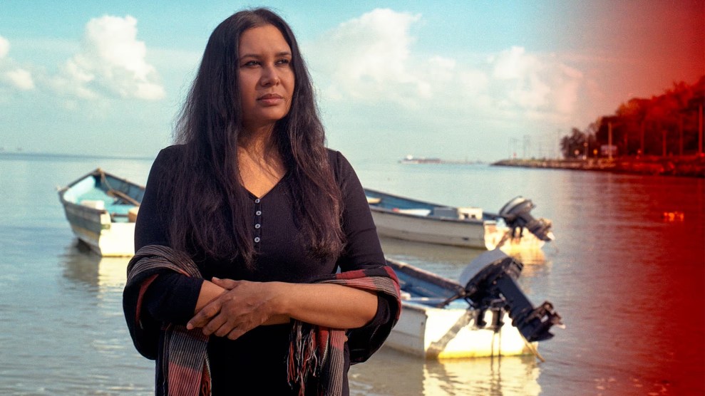 A woman with brown skin and black hair standing in front of a boat in water
