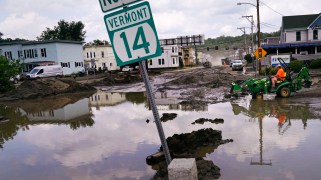 A small tractor clears water from a business as flood waters muddy a street.