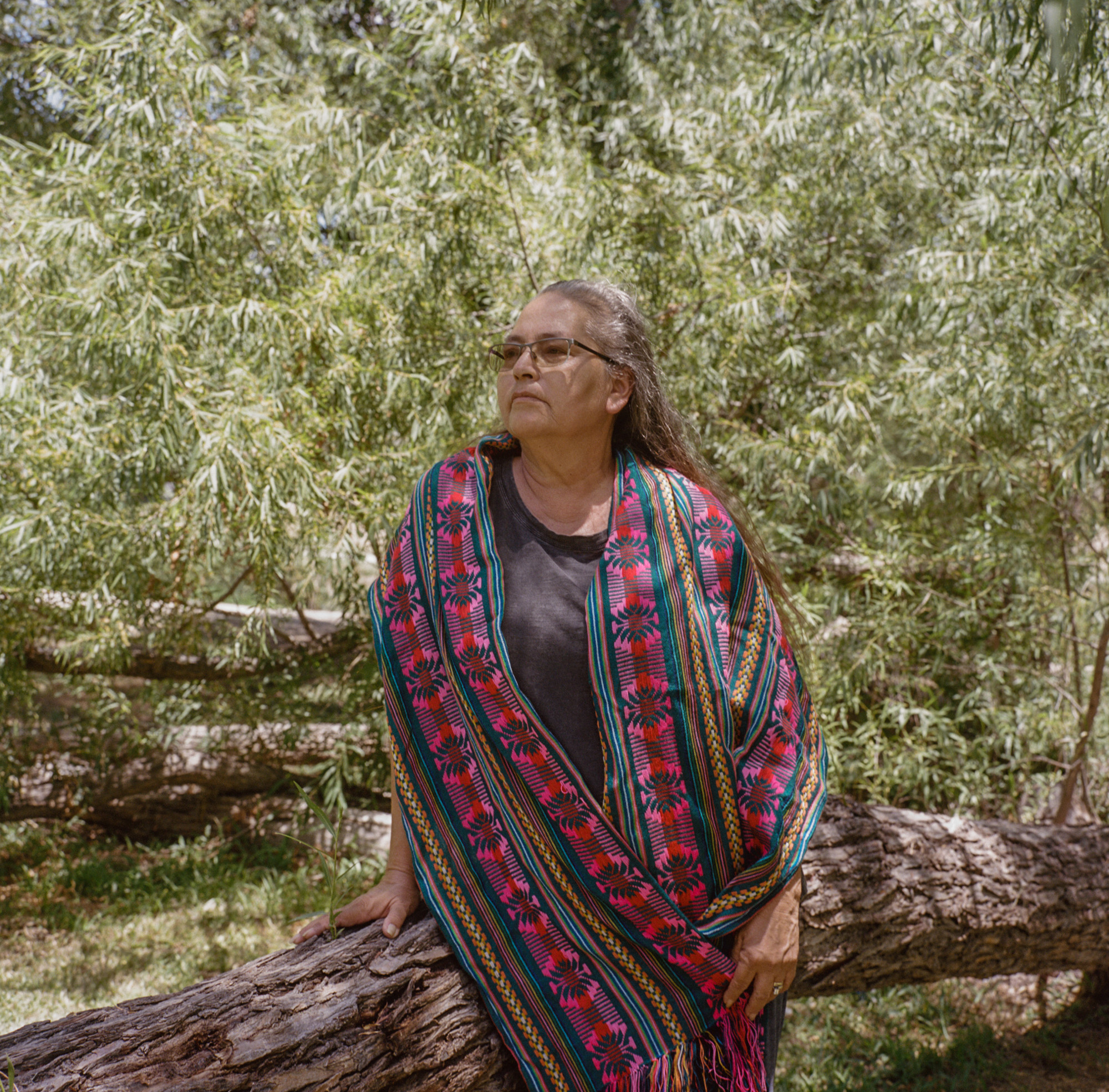 Portrait of a woman standing outside under the shade of trees.