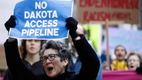 A person with short grey hair holds up a sign that says "No Dakota Access Pipeline"