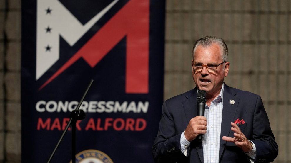 Rep. Mark Alford speaking into a microphone in front of a red, white, and blue banner with his name.