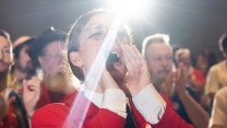 Woman in red with hands cupped around her mouth, yelling.