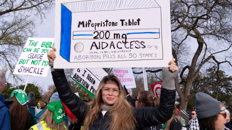 A woman holding up a hand-drawn sign depicting a box of mifepristone tablets at an outdoor protest for abortion rights in Washington, DC.