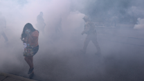 A woman in a mask walks through a cloud of tear gas.