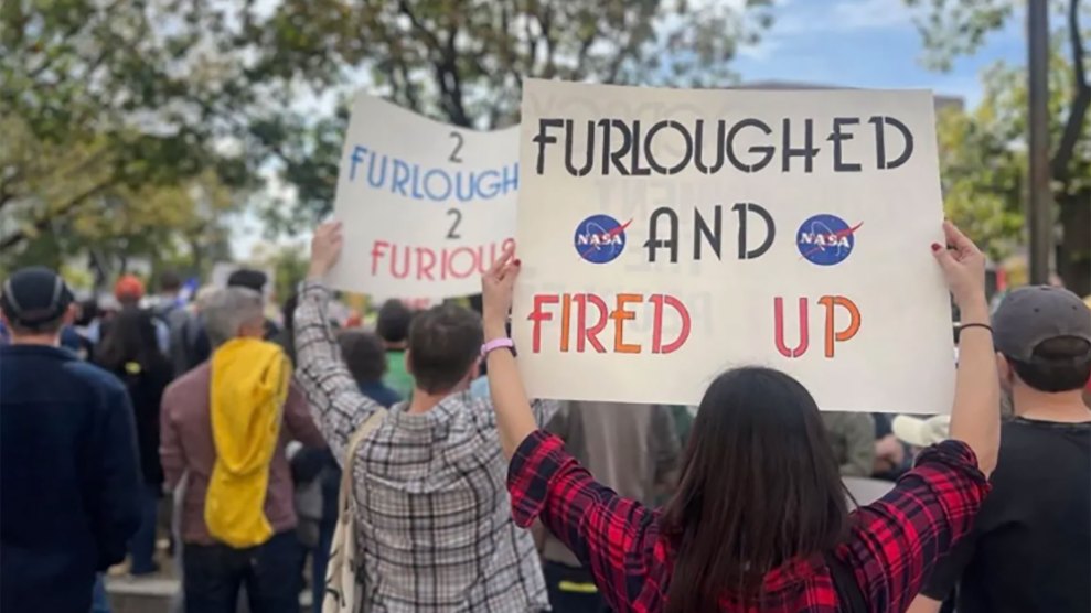Workers at a protest face away from the camera and hold signs saying Furoughed and Fired Up, and 2 furoughed 2 furious.