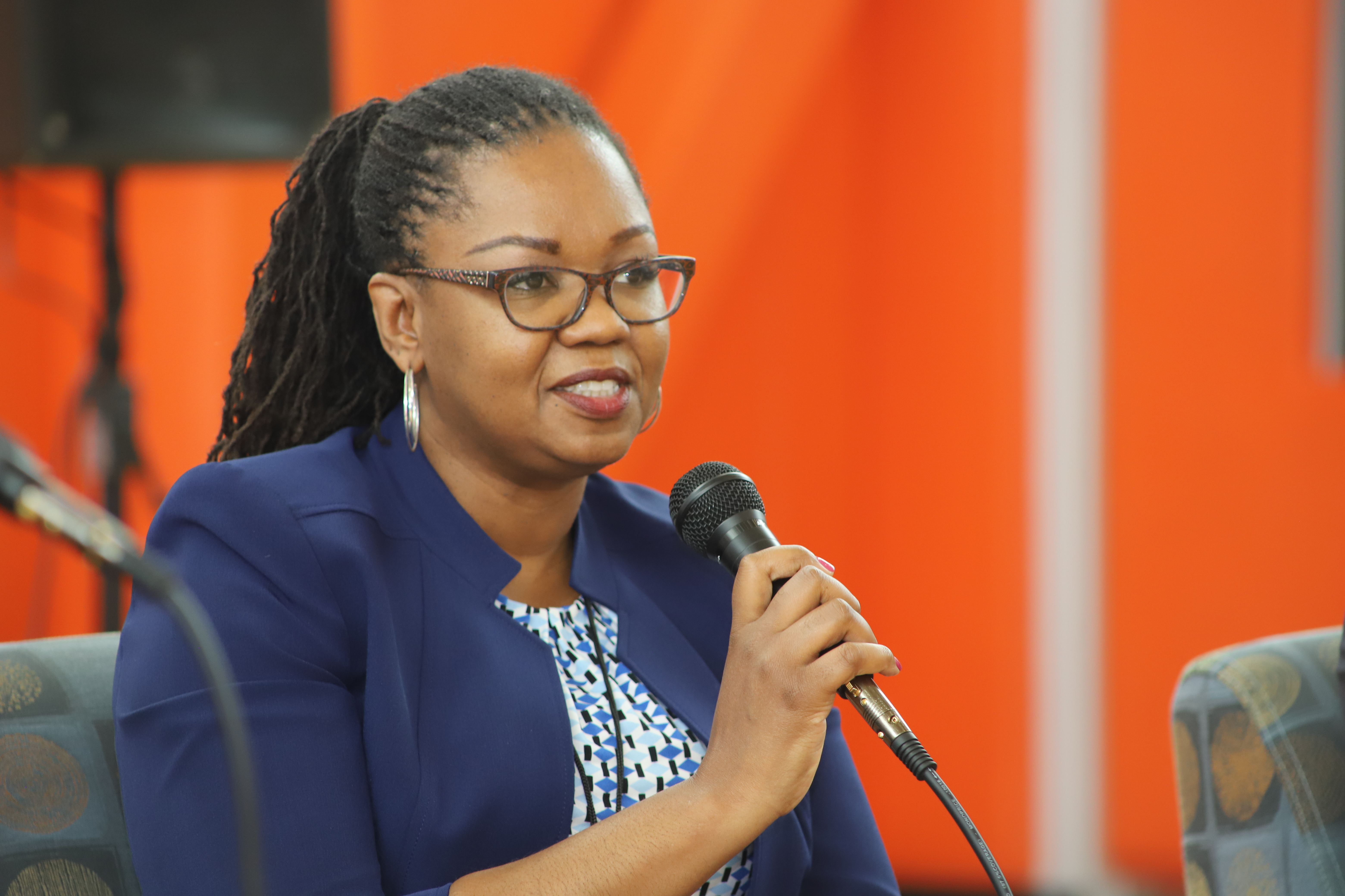 Jamila Hodge, a bespectacled African American woman speaks into a microphone