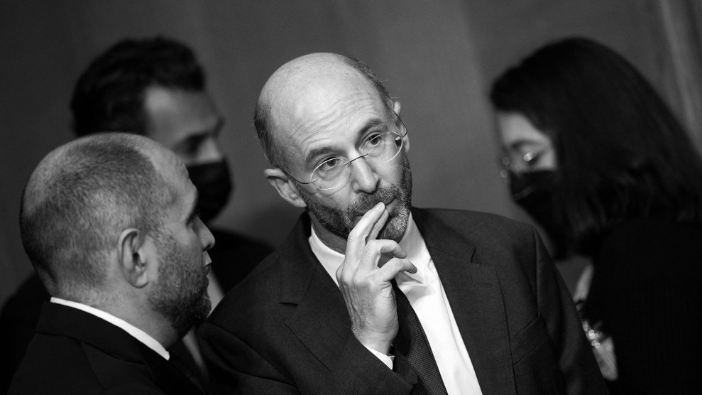 Two men talking. One man in glasses holds his hand to his mouth.