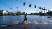 A person walks on a cross walk that is ankle deep flooded in water.