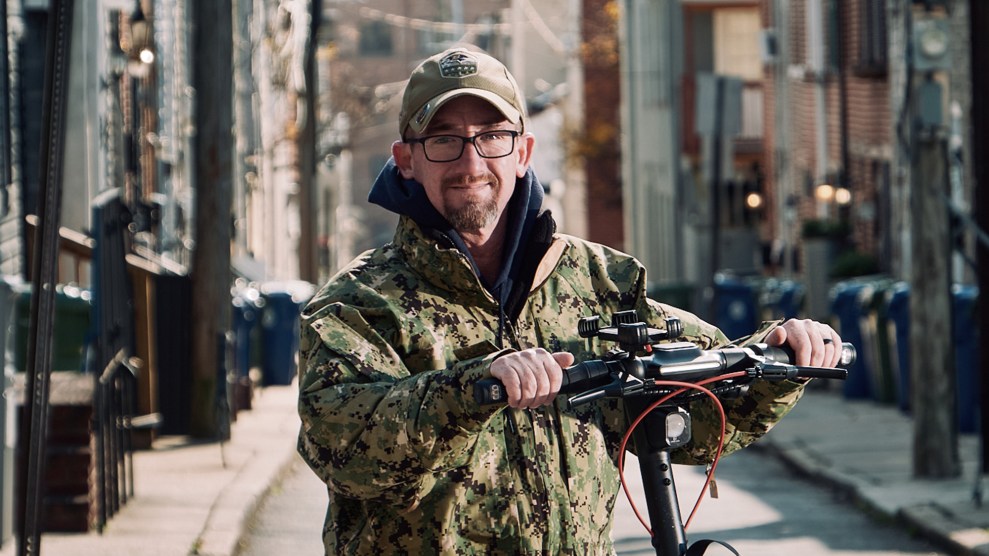 Man wearing camouflage, standing on an electric scooter.
