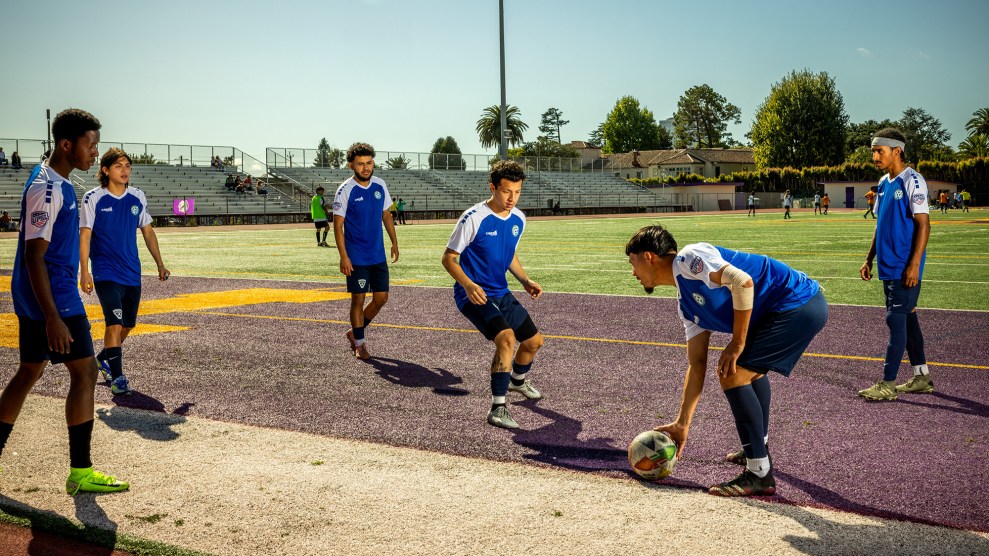 Six young men in blue and white jerseys practice on an astroturfed soccer field during the day.