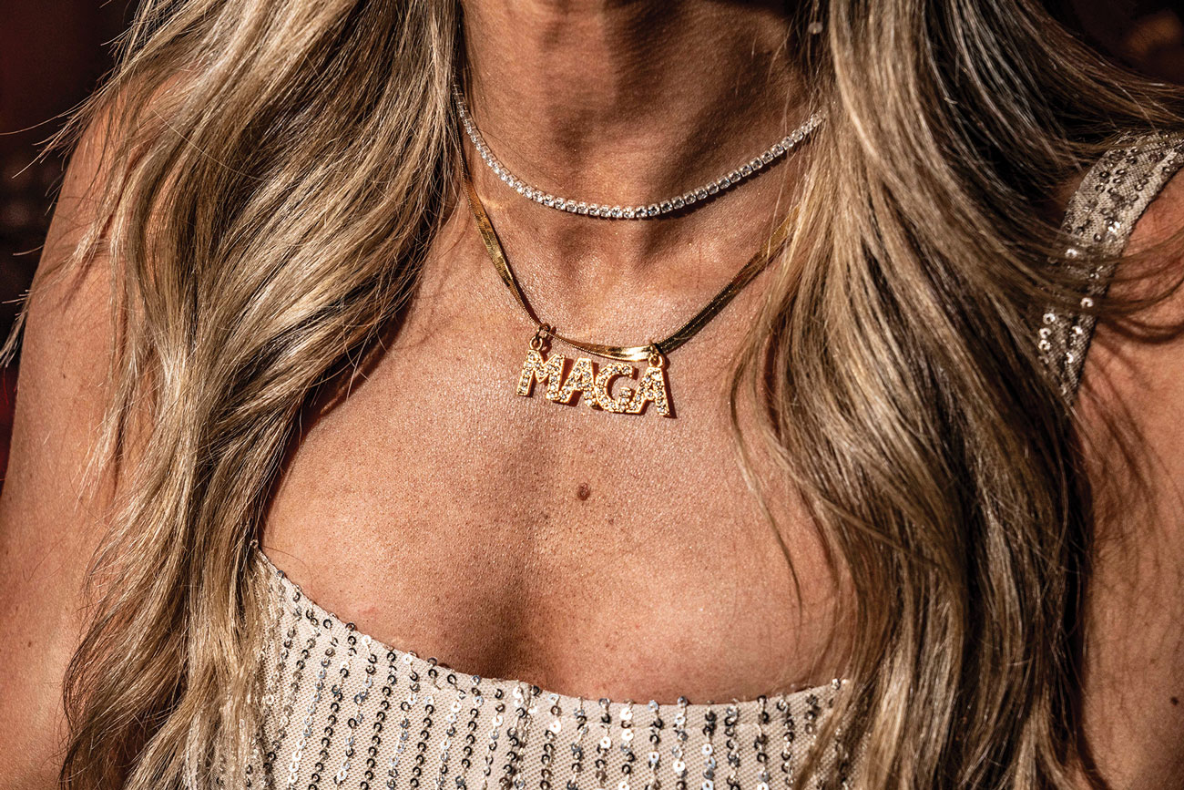 The neck and upper chest of a woman wearing a gold sequined dress and a gold necklace with a pendant that reads, “MAGA.”