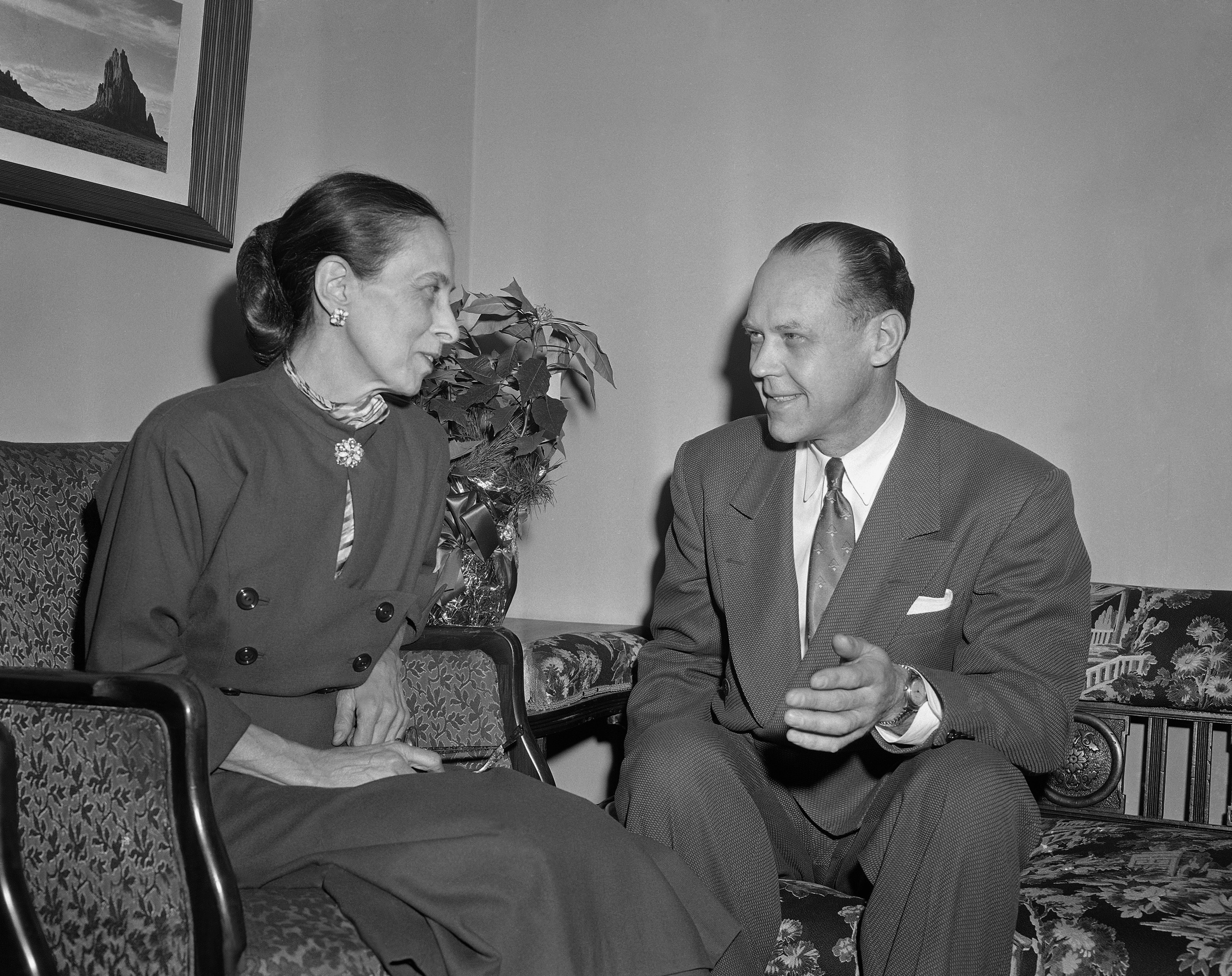Archival photo of Dorothy Martin, a housewife in a nice dress, talking and smiling in a living room with Dr. Charles A. Laughead, a middle aged man in a suit. 