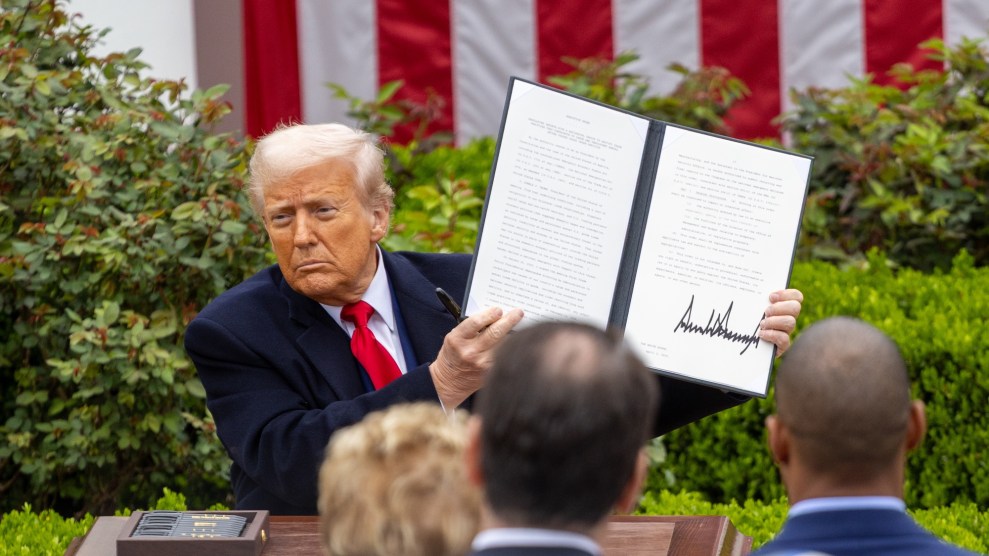 Trump sits at a desk outside the White House, holding up a two page document he just signed.