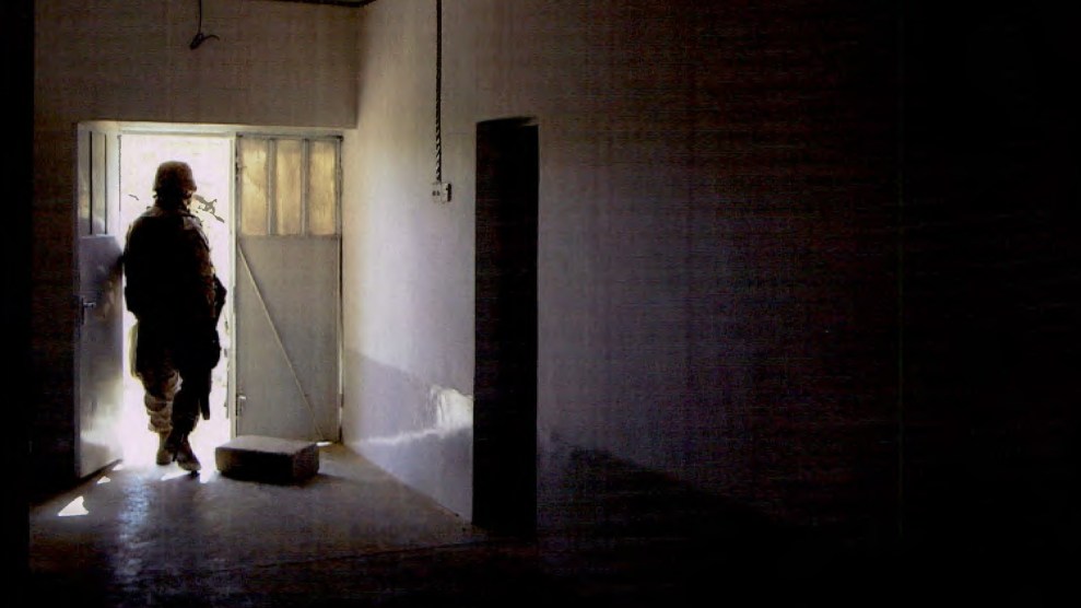 At the end of a dark hallway, a Marine steps through a doorway. His silhouette is dark against the bright outside light.