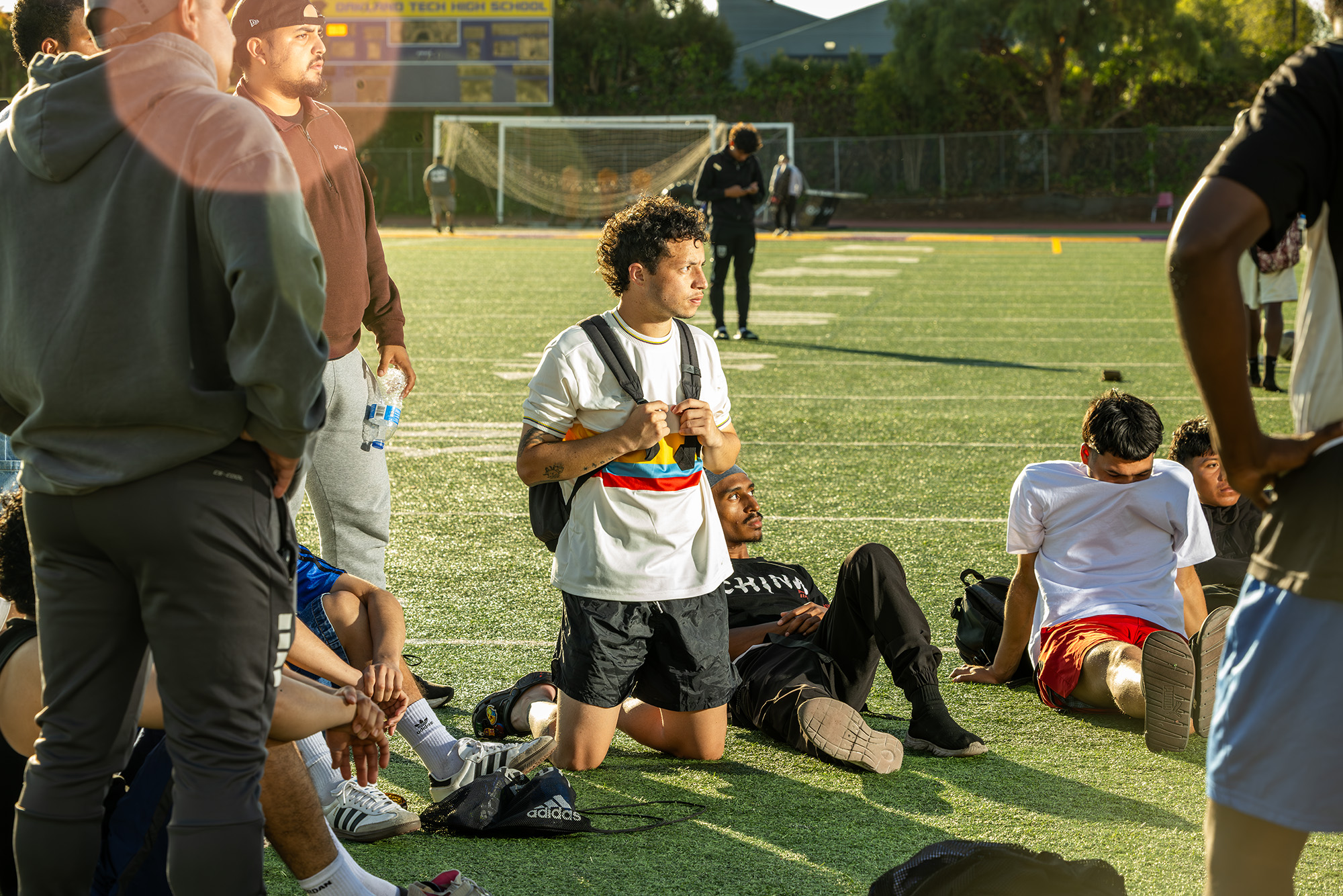 Dilan Pinzón kneels on an astroturfed field among a group of young men. He clutches the straps of his backpack.