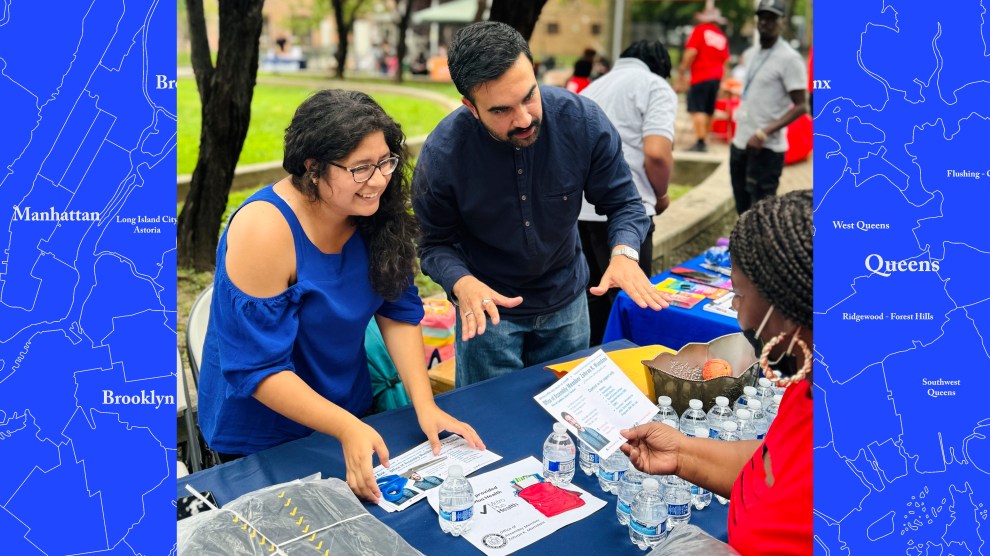 Photo of Zohran Mamdani, a young bearded man, and Mariela Ortiz, a young woman with glasses and dark hair, interacting and talking with a community member at an outdoor event.