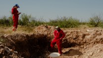 Sarah Stogner and Hawk Dunlap stand in red boiler suits investigating an abandoned oil well.