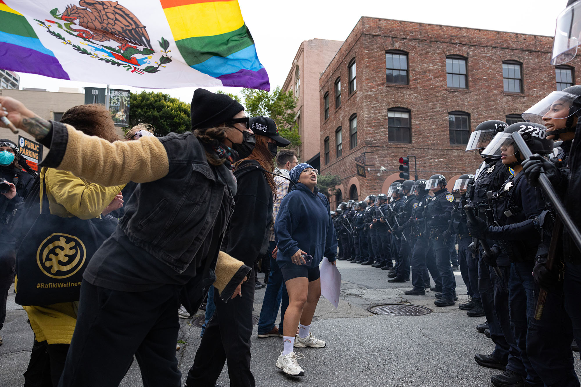 A line of protesters stands in a street facing a line of San Francisco police officers wearing riot gear.