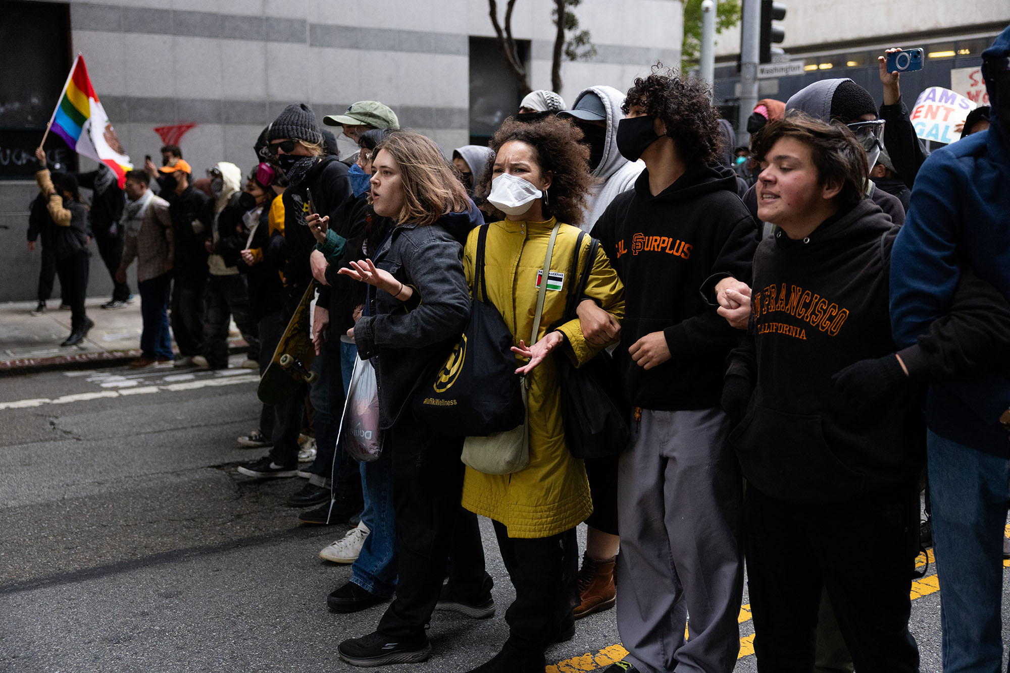 Line of protesters march arm in arm down a city street.