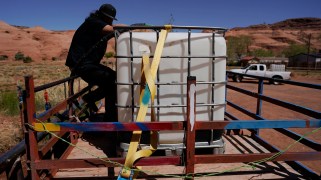 A person wearing a black shirt and black pants straps a water tank in the back of his truck.