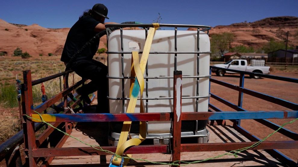 A person wearing a black shirt and black pants straps a water tank in the back of his truck.
