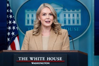 Karoline Leavitt standing on a podium during press briefing wearing a tan jacket.