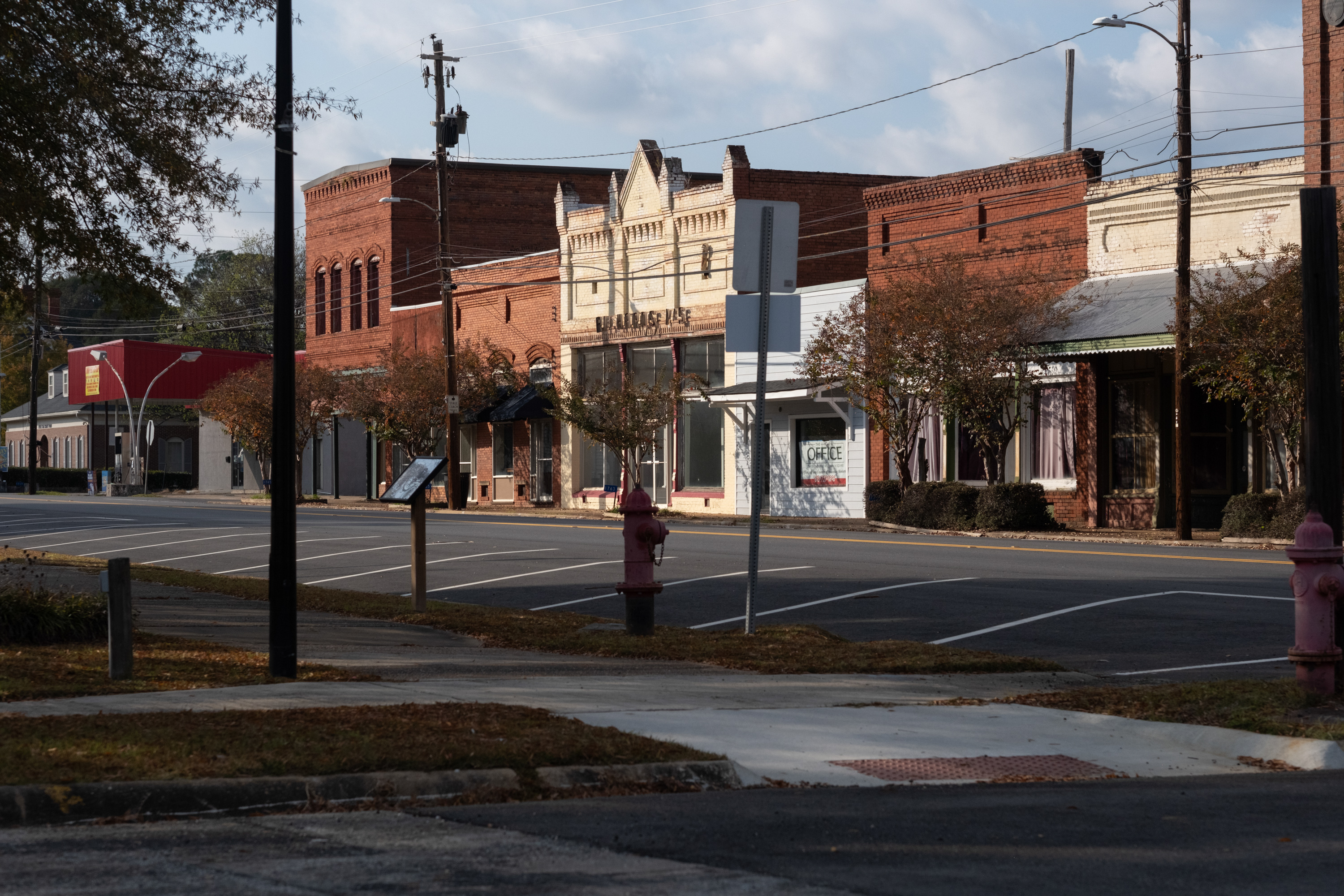A view of Lumpkin's downtown, which is composed of small brick buildings, including three red ones, two white ones and a pale blue one. All of the parking spaces in front of the buildings are empty.
