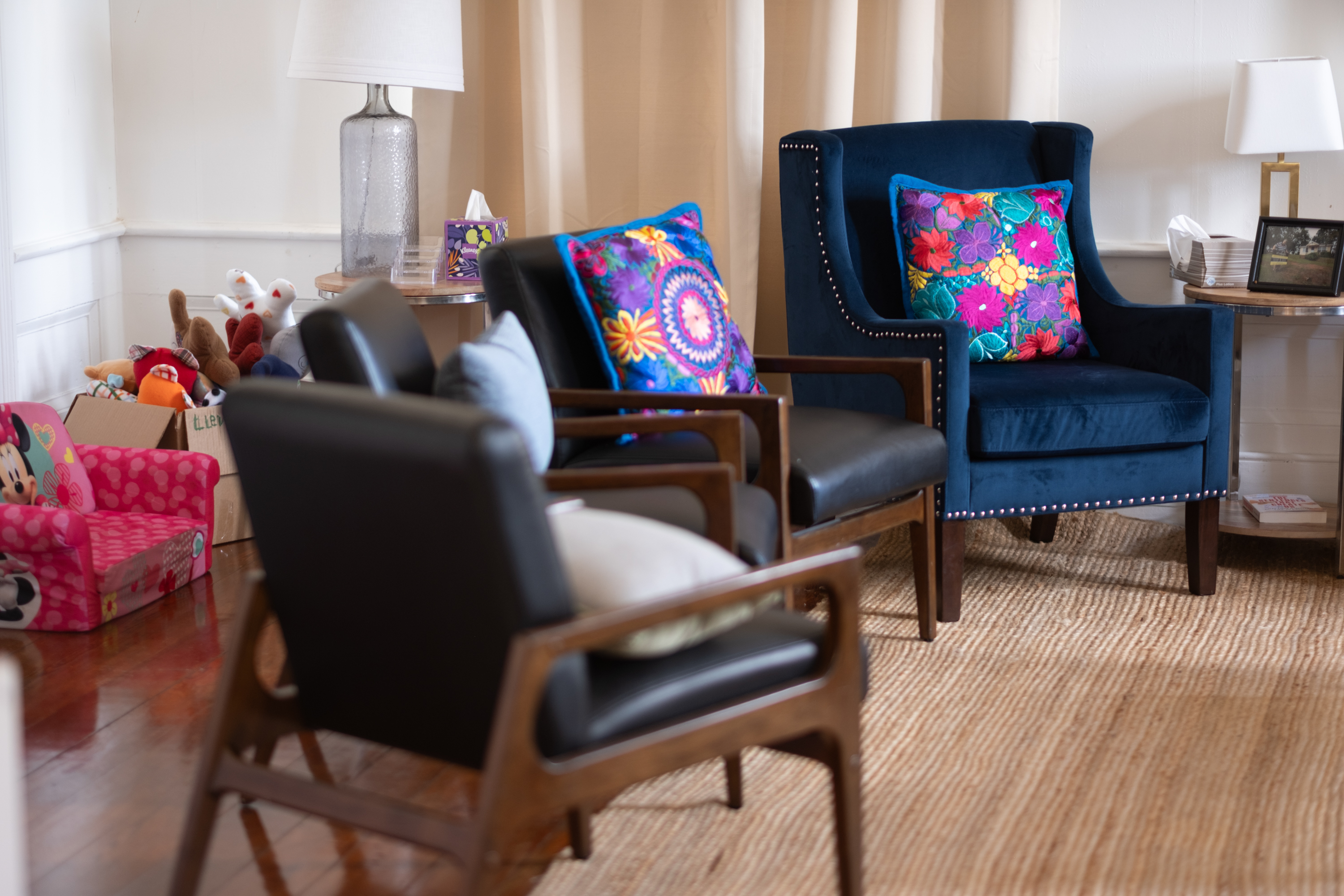 Three leather and wooden chairs and one blue velvet chair are arranged in a curve. On two of the chairs are bright, multicolored embroidered pillows.