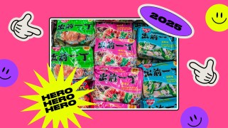Rectangular photo of packages of instant ramen noodles in a frame with a white border on a pink background. Various stickers are layered on top of the frame and background, including one that reads "HERO" over and over, "2025", two hands pointing inward, and purple and yellow smiley faces.