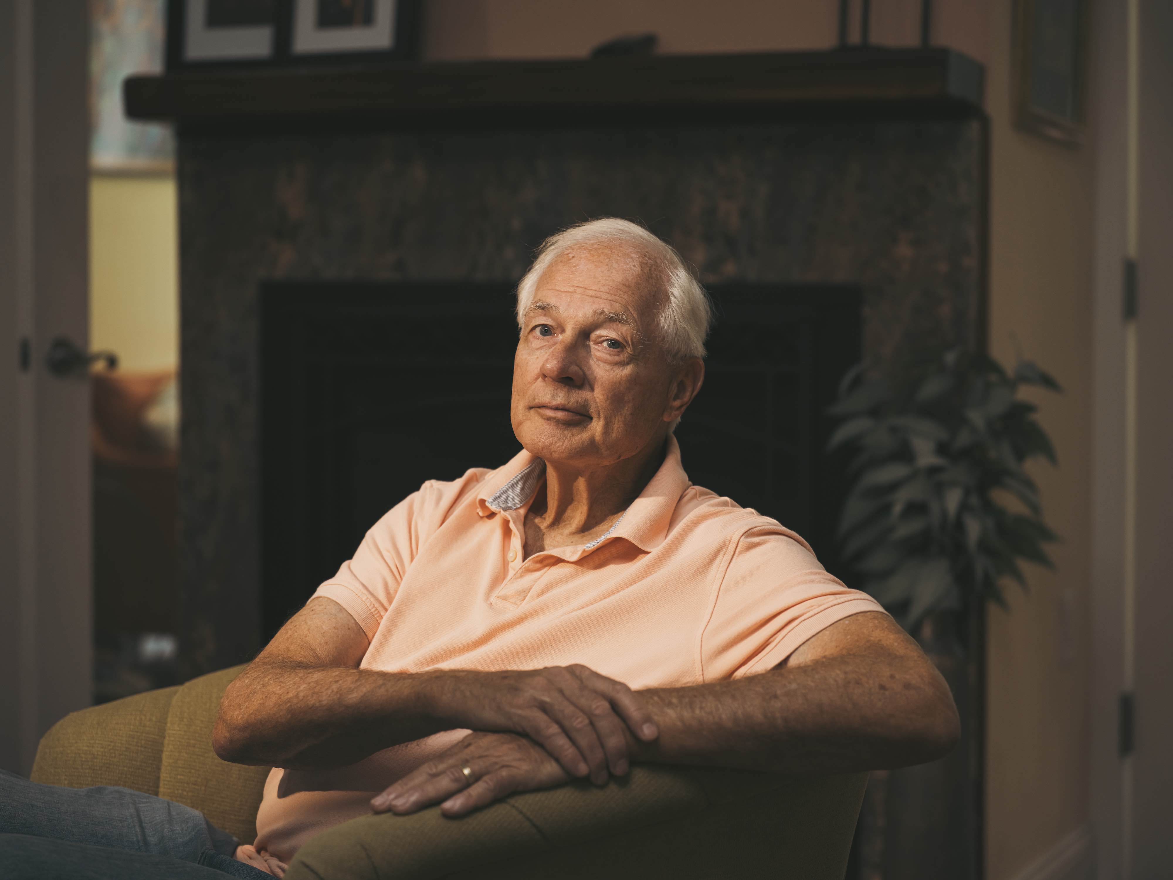 A white man, with white hair, wearing a salmon polo shirt.
