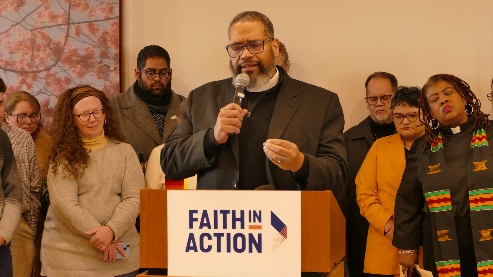 Clery listen on as Bishop Dwayne Royster prays for those impacted by ICE's actions.