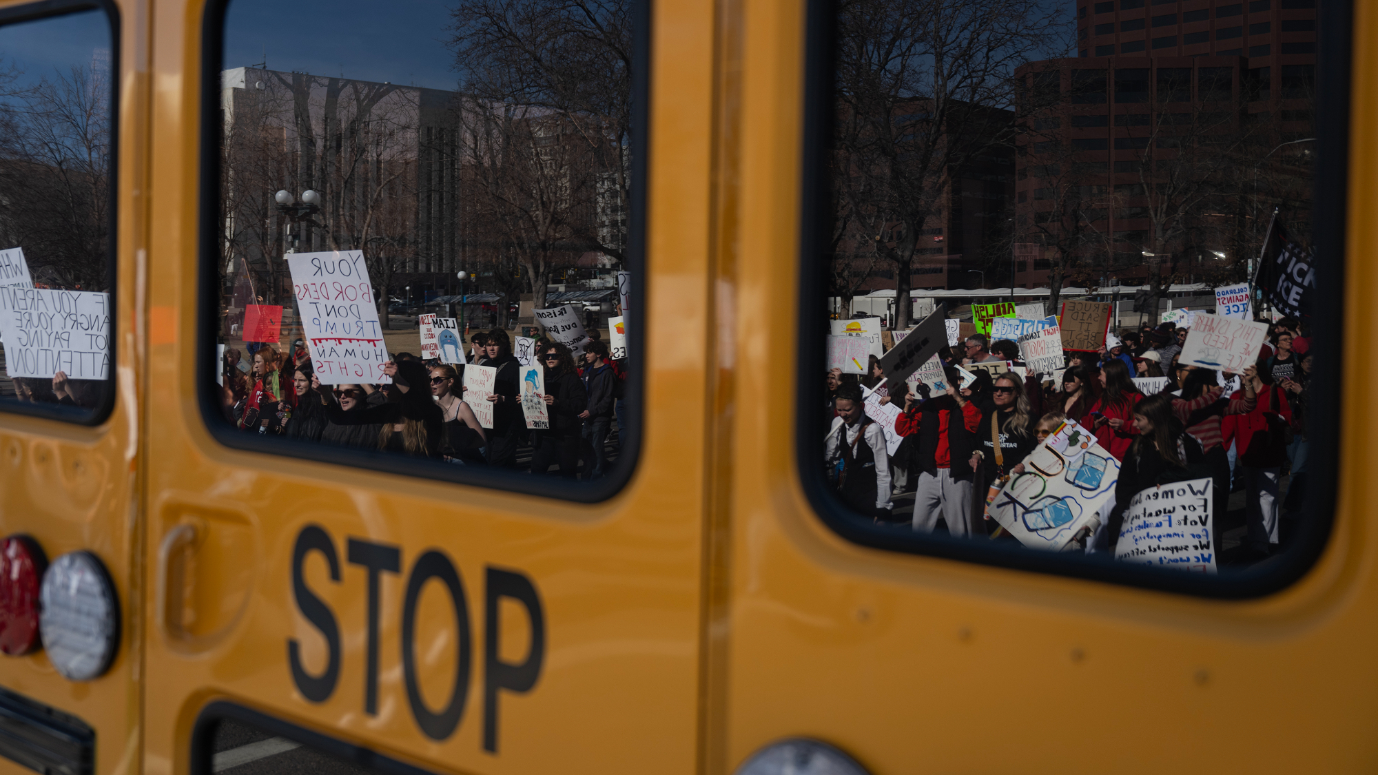 Protesters seen in the reflection of a school bus that says "STOP"