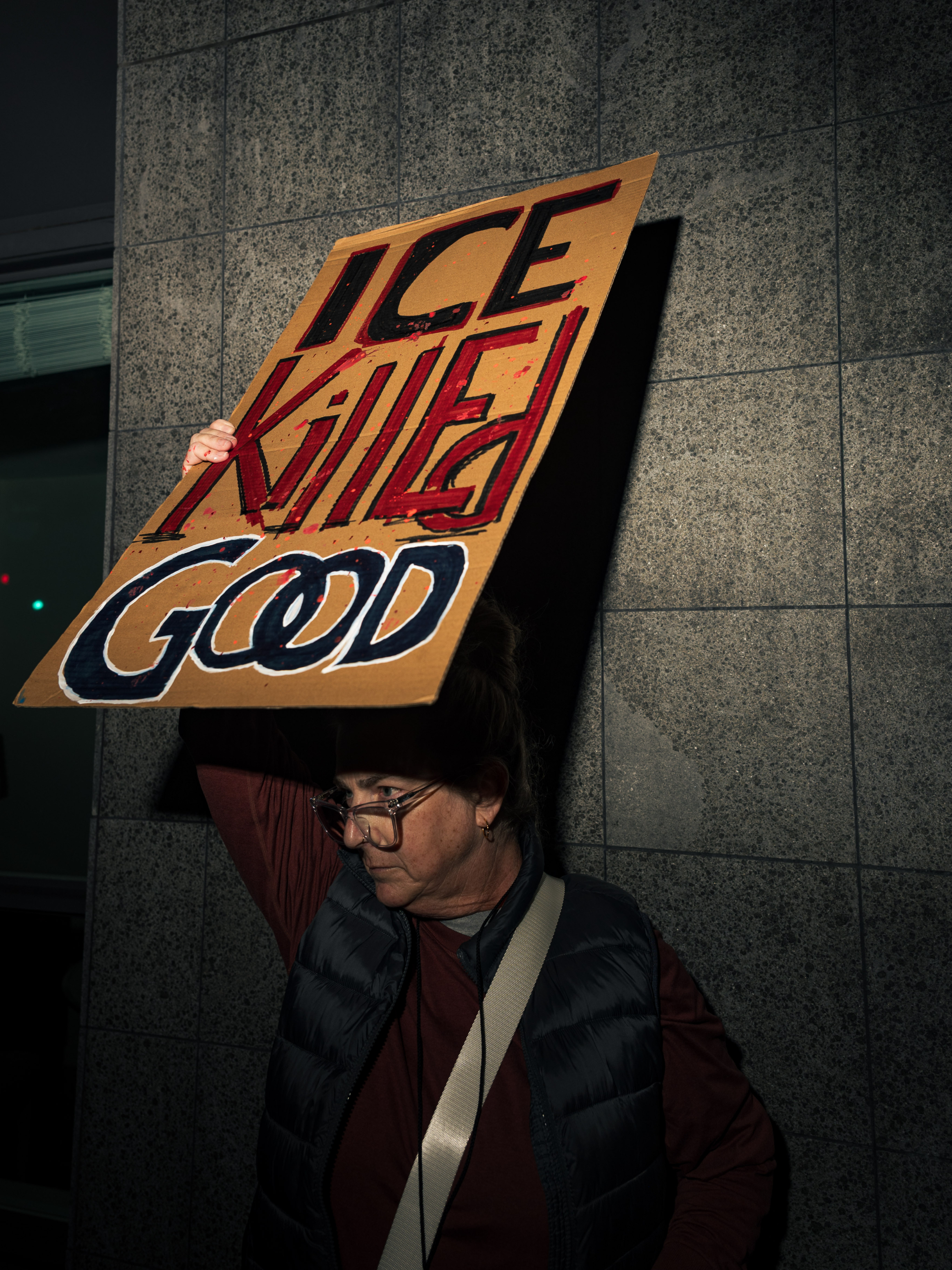 A white person holding up a cardboard sign that says "ICE killed Good."