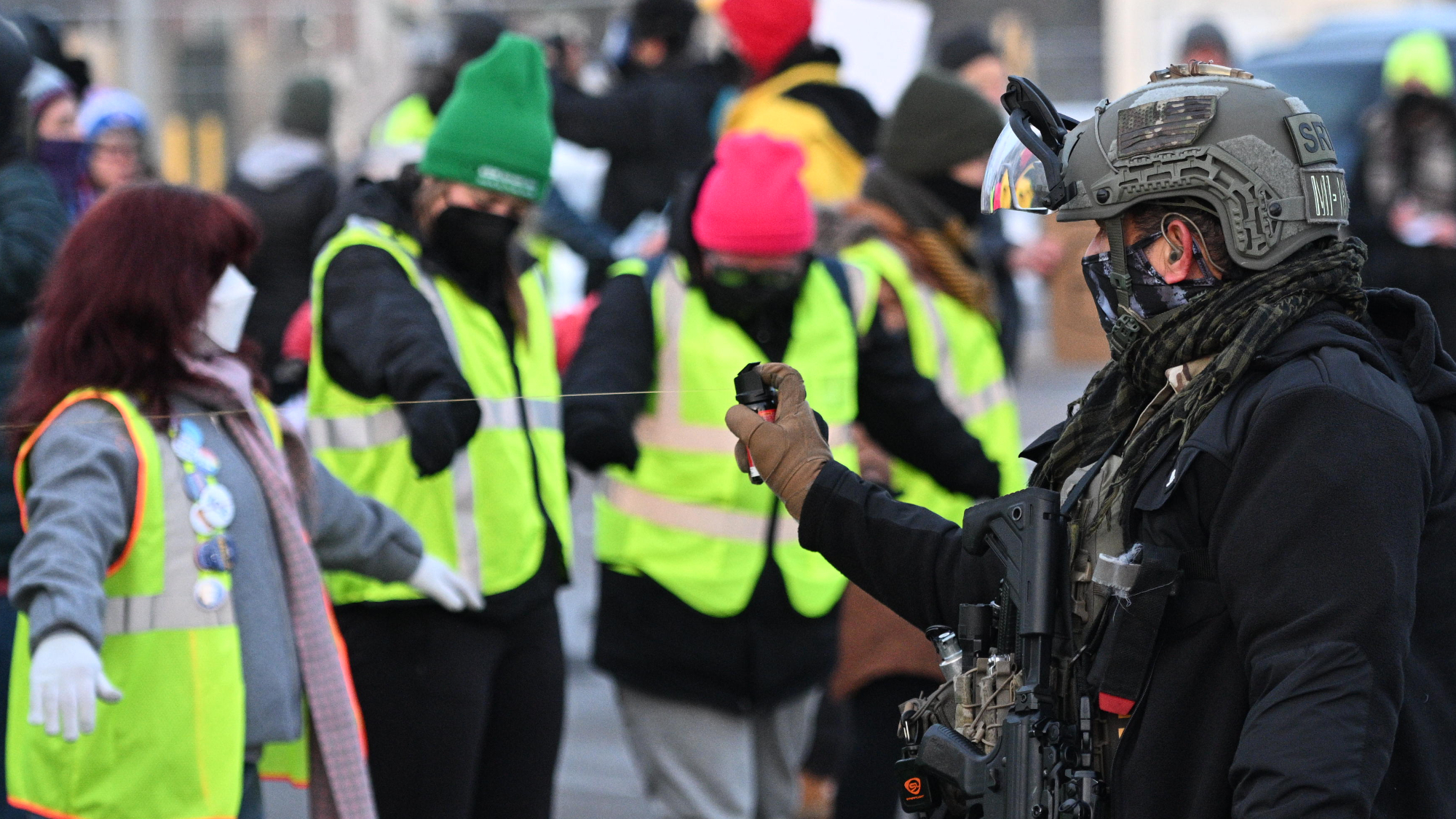 A police officer user chemical agents on people. There's a row of masked protestors in the front.