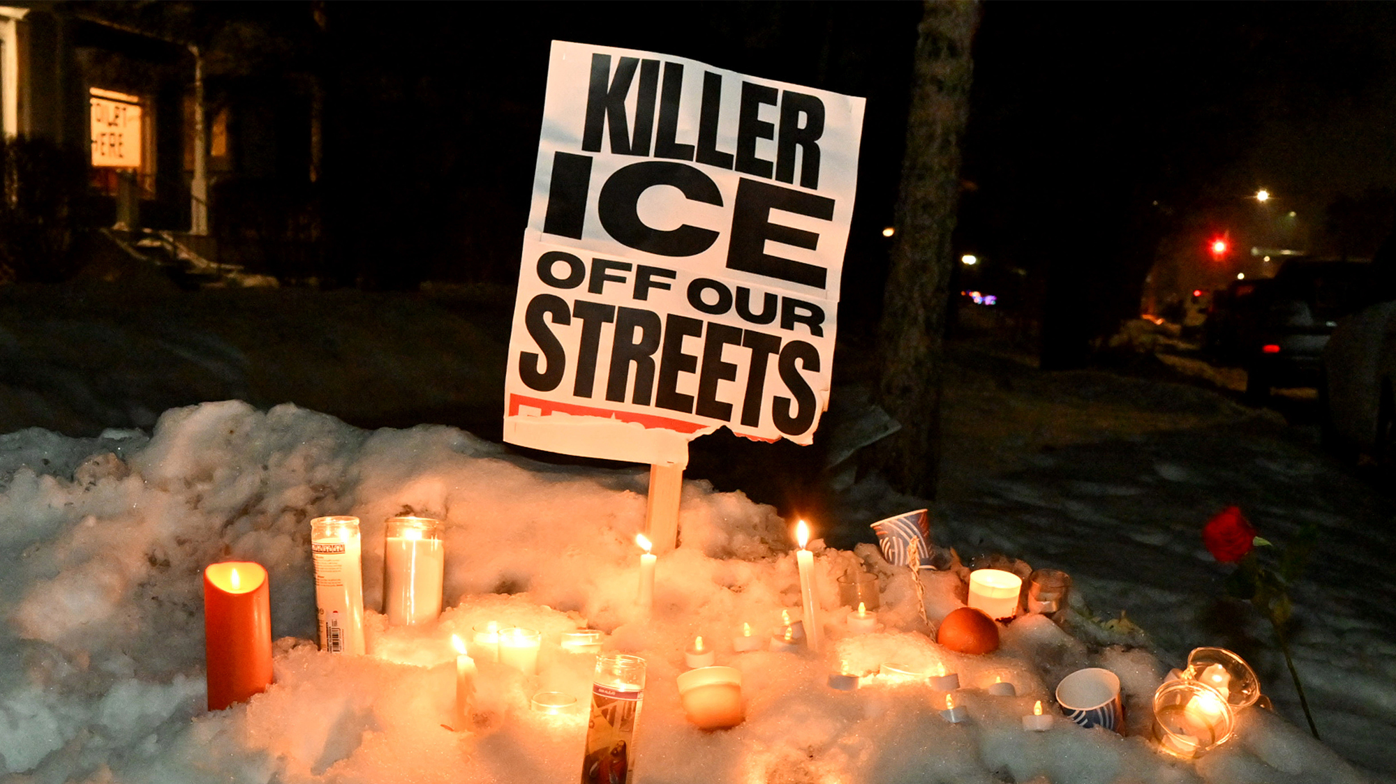 Candles placed in the snow as a vigil for Renee Good; behind is a sign that reads "KILLER ICE OFF OUR STREETS"