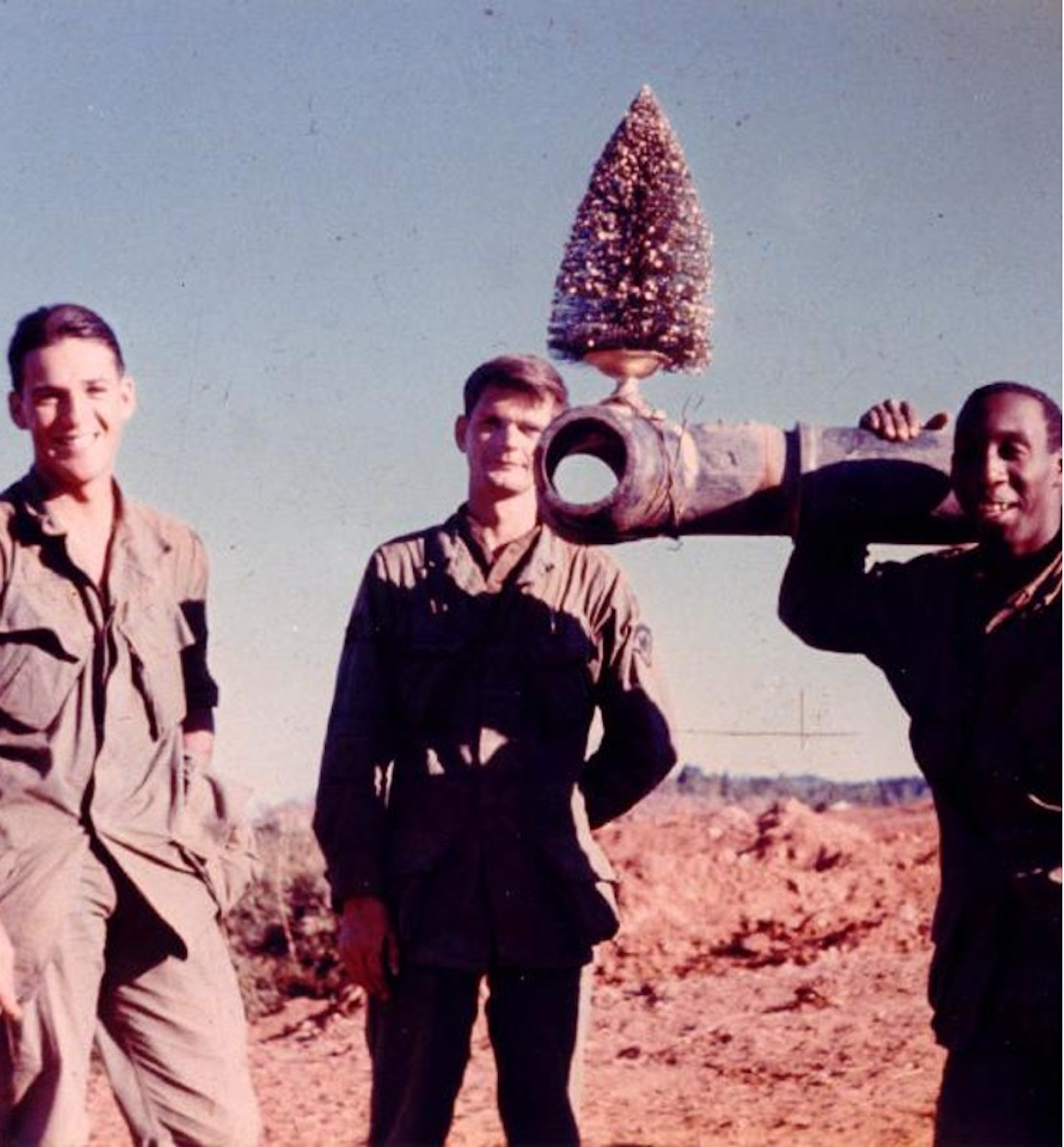 Three men stand near a tank barrel with a small Christmas tree on it.
