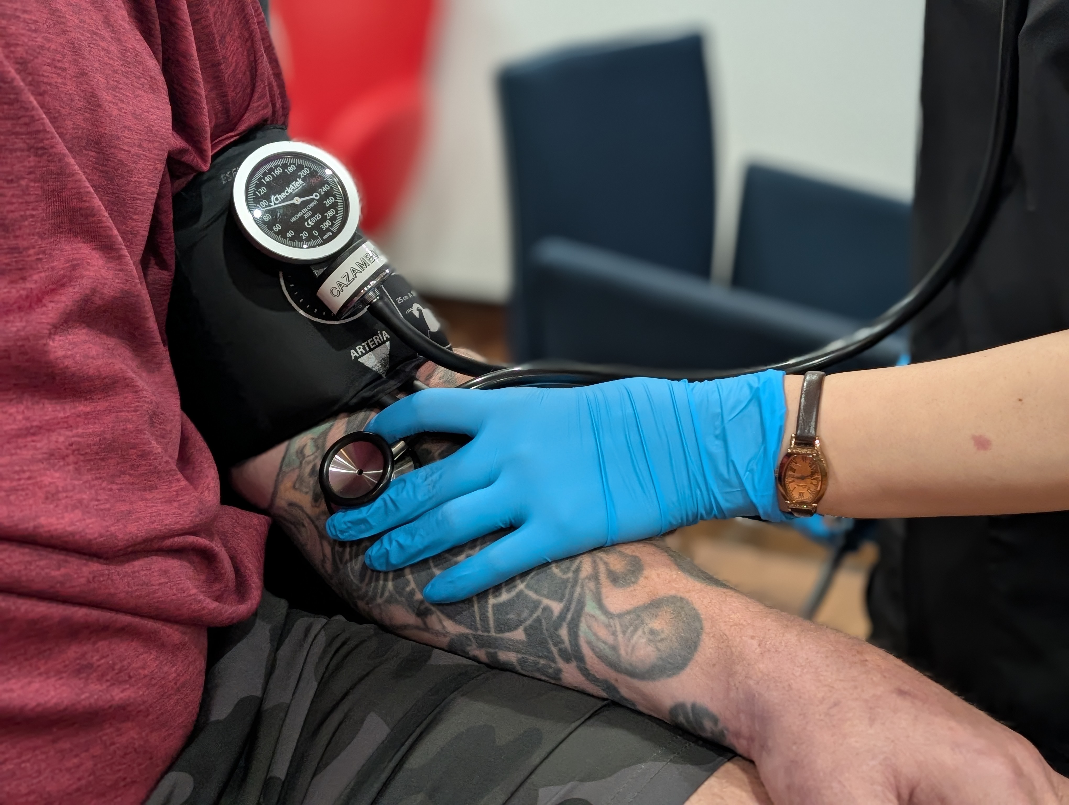 Close-up of a nurse checking the blood pressure of a heavily tattooed man.