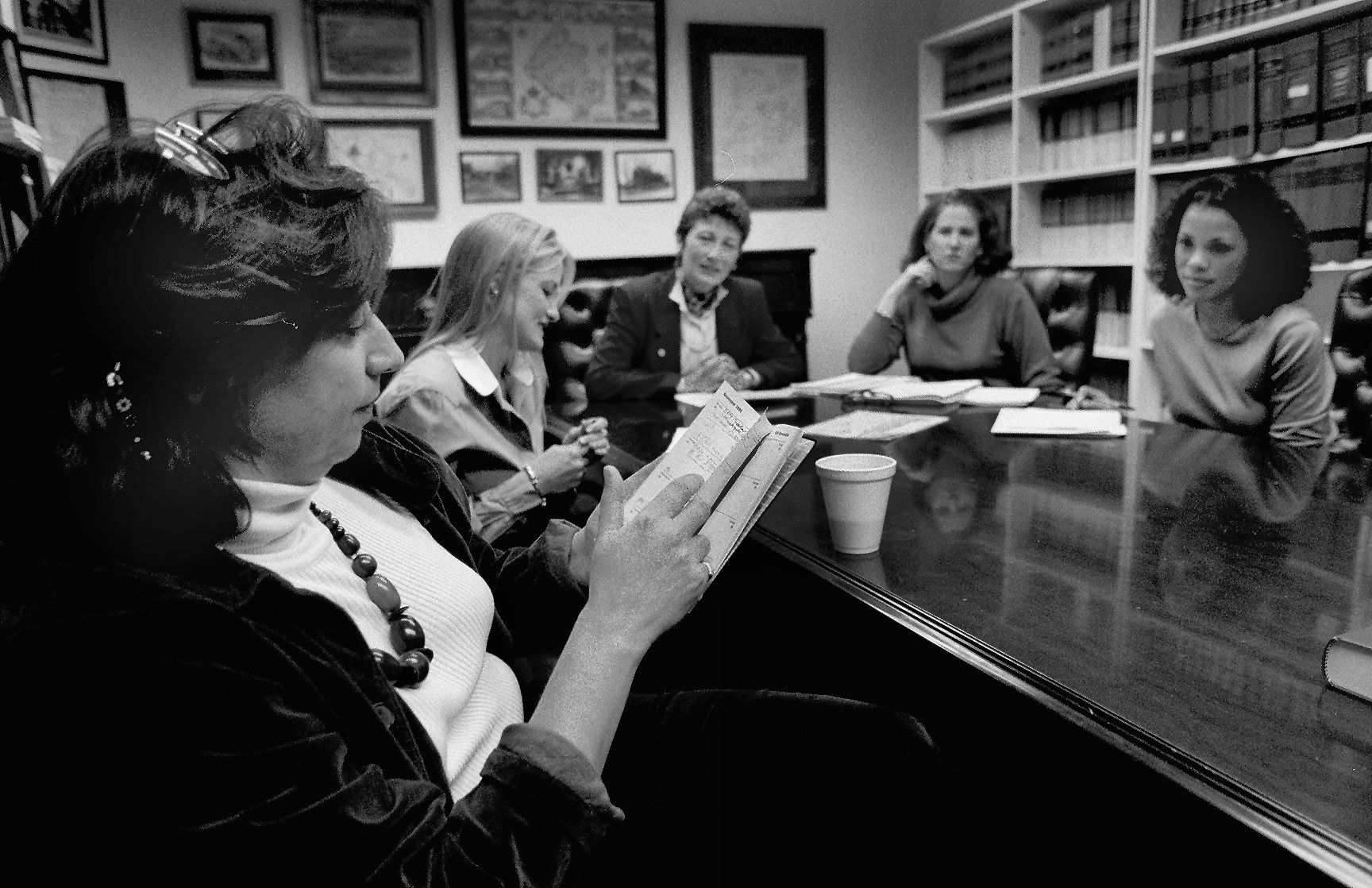 Black-and-white archival photo of five white women in discussion around a meeting room table.
