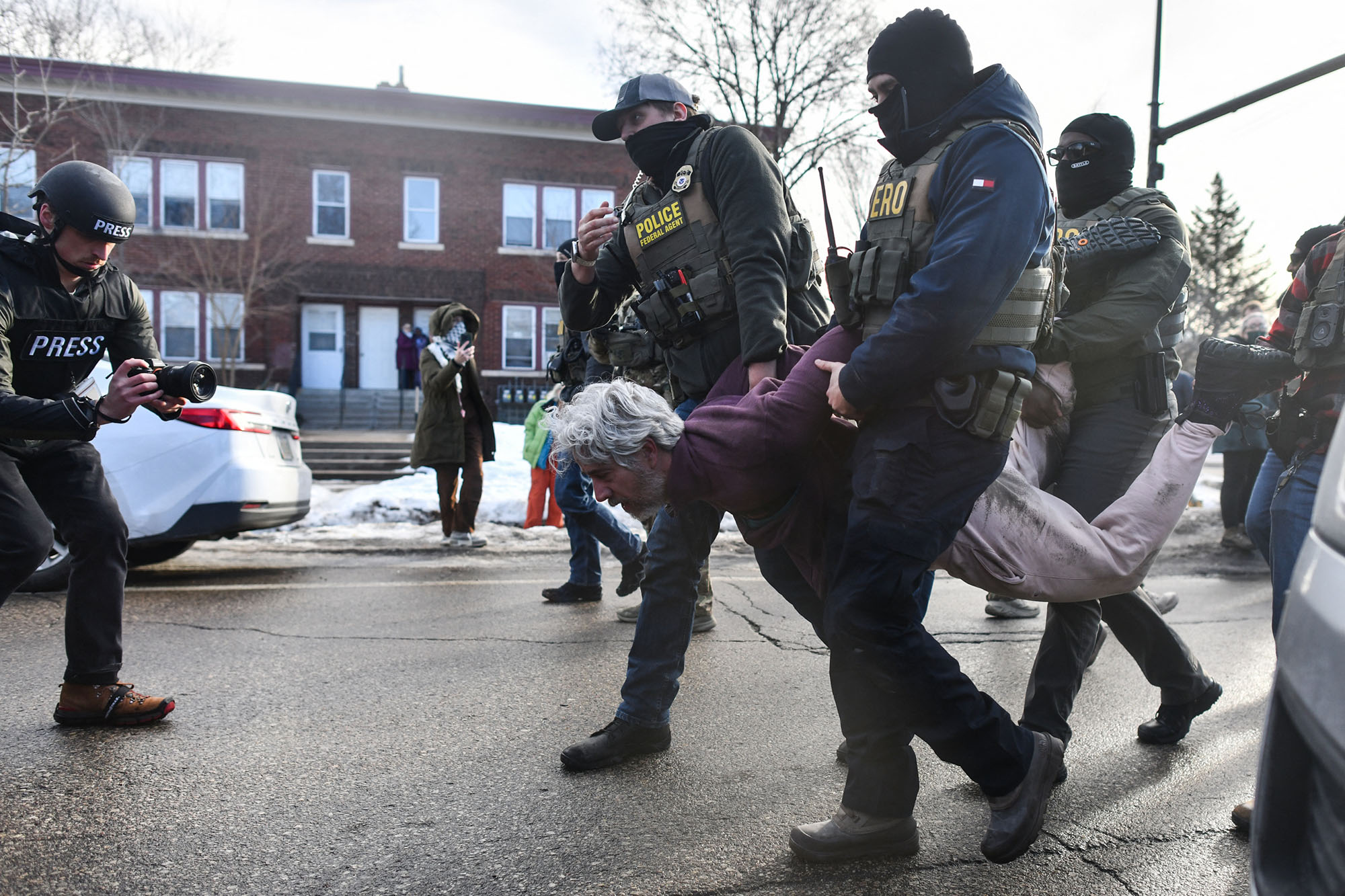 Federal agents carry a hogtied man down the street.