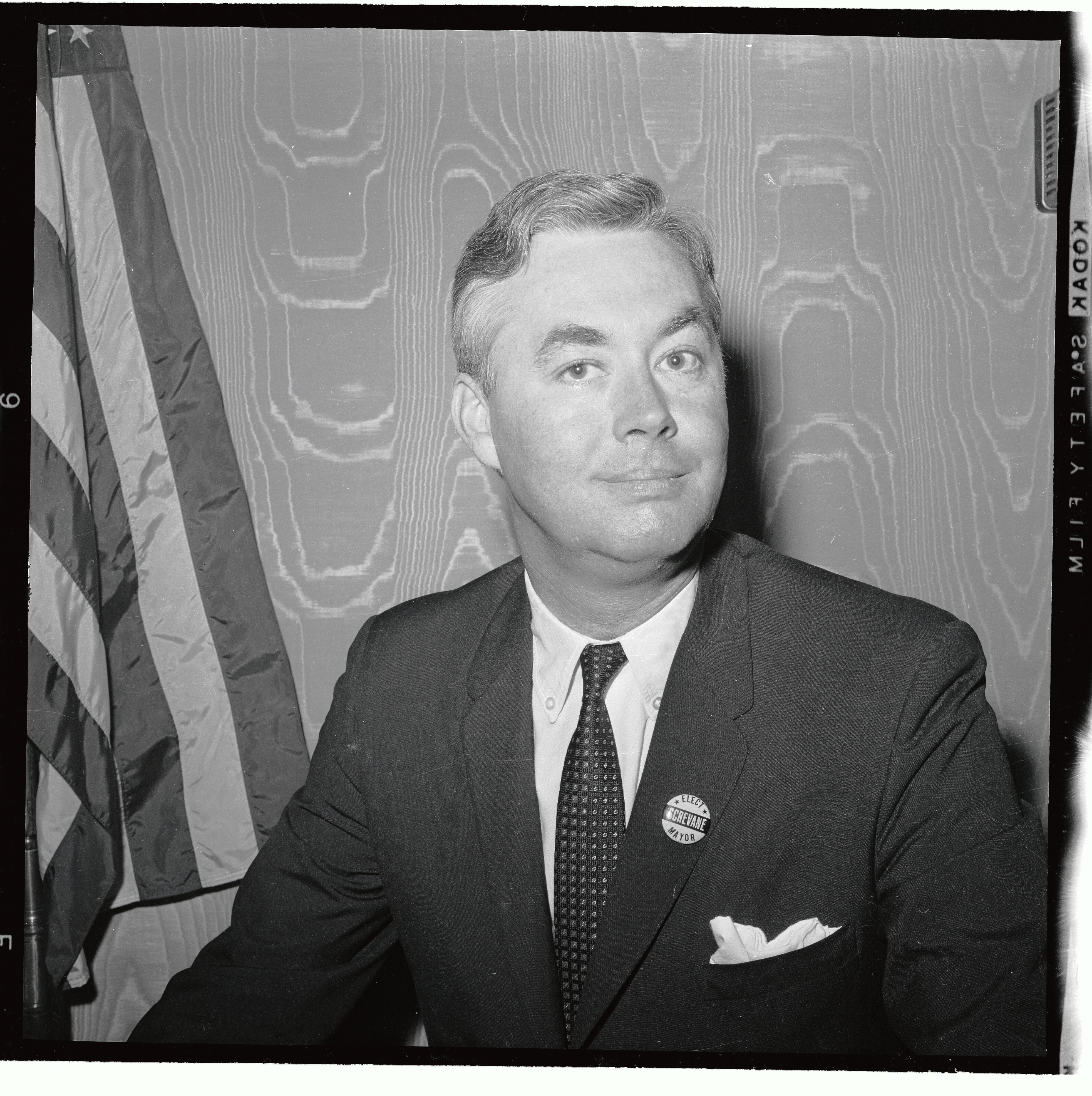 Portrait of white man in a suit next to American flag.