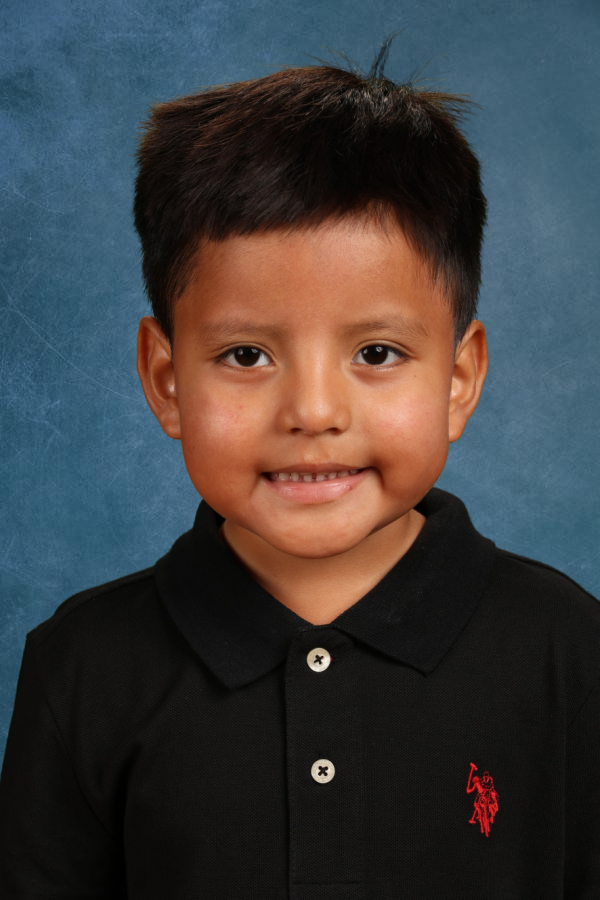 A young boy smiles in a school portrait wearing a black polo shirt. 