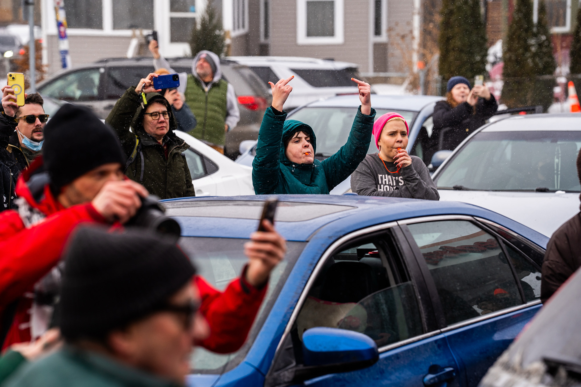Group of people, most holding phones, with one prominent woman flipping a double bird.