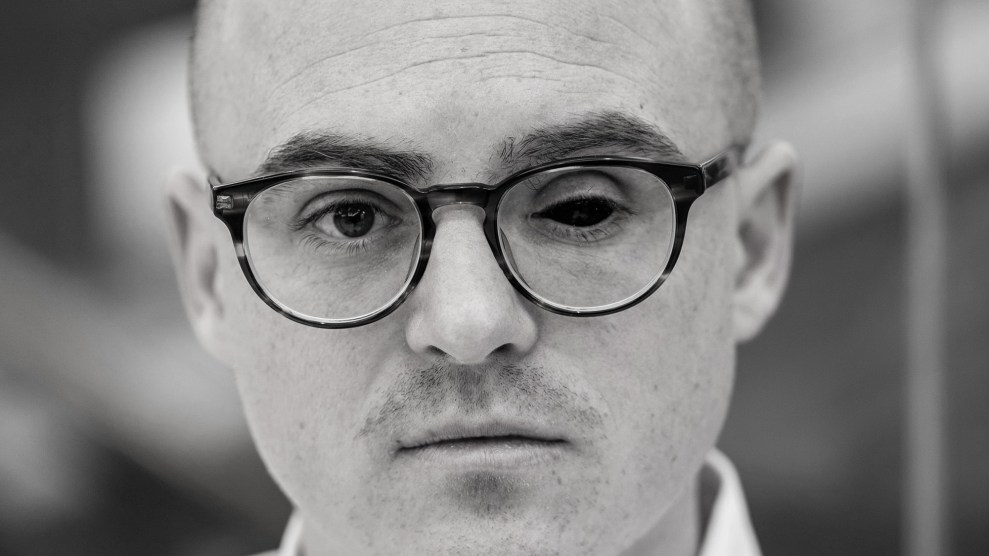 Black and white close-up portrait of man wearing glasses, missing one eye.