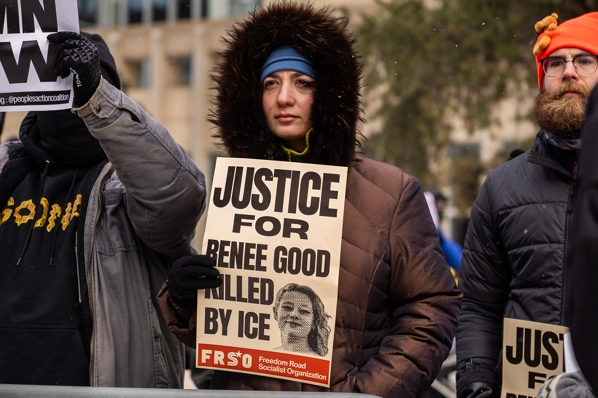 A woman in a winter coat holds a sign that reads, "Justice for Renee Good, Killed by ICE."