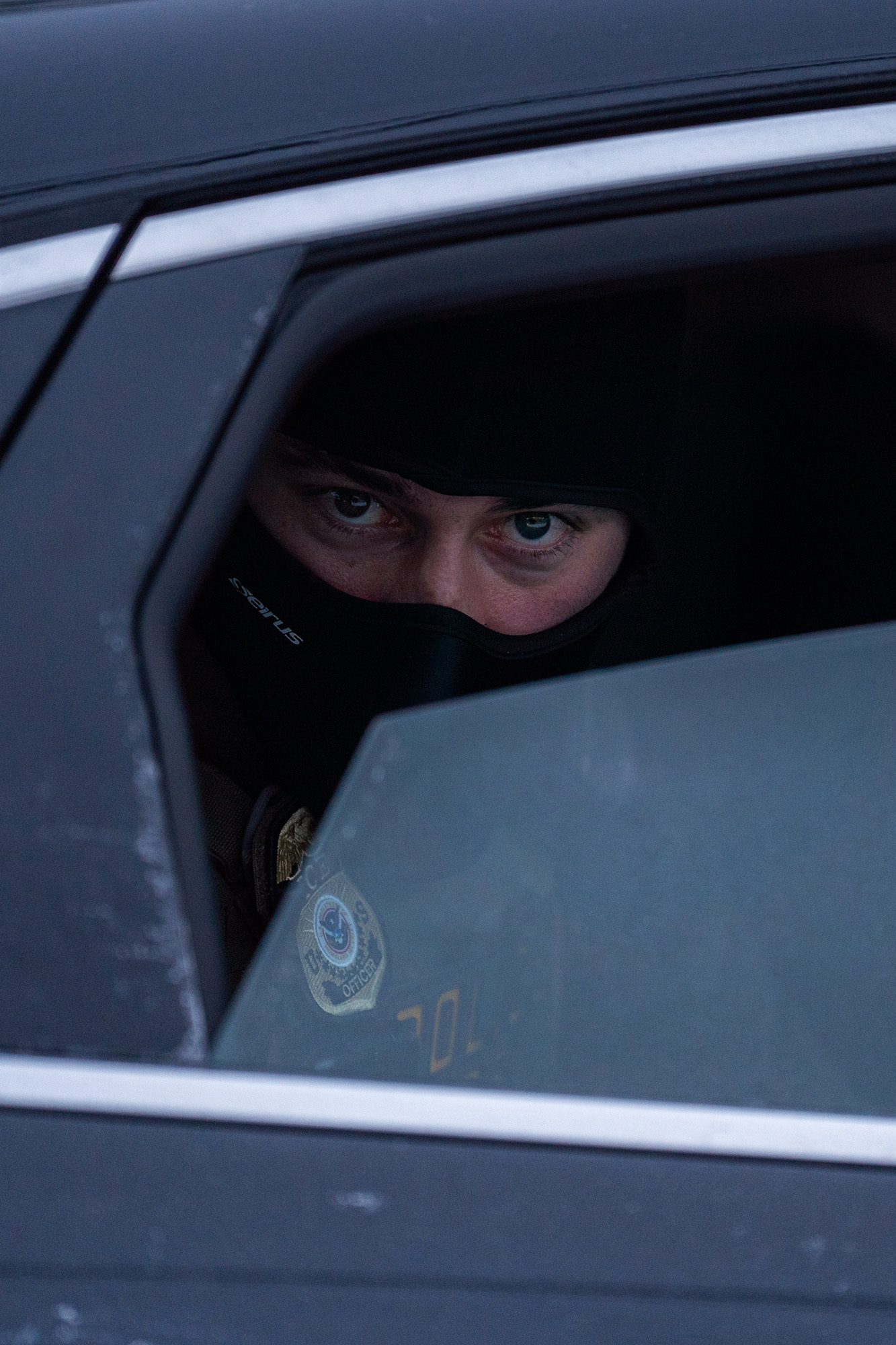 Close up of a masked federal agent looking out of a car window.