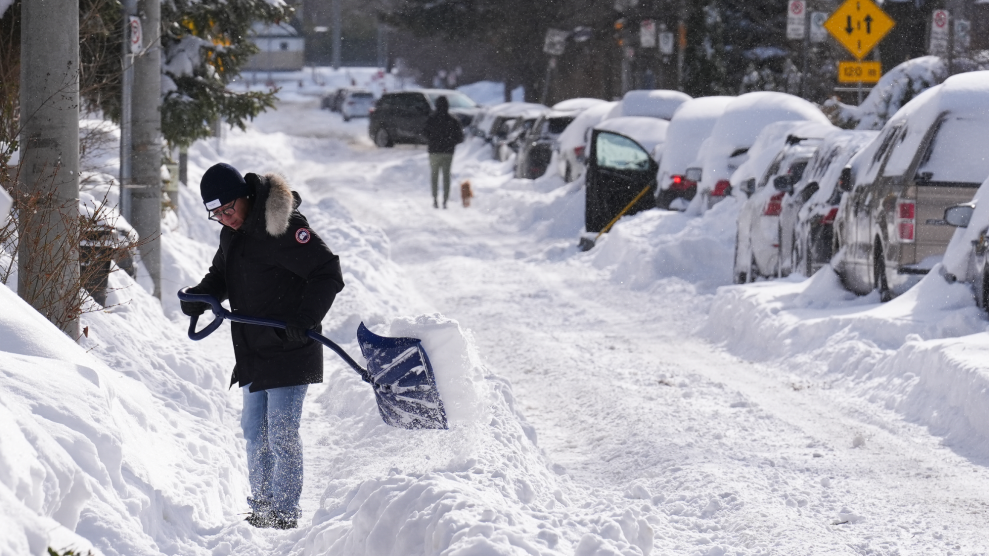 A person wearing a black jacket shovels out a car buried in snow.