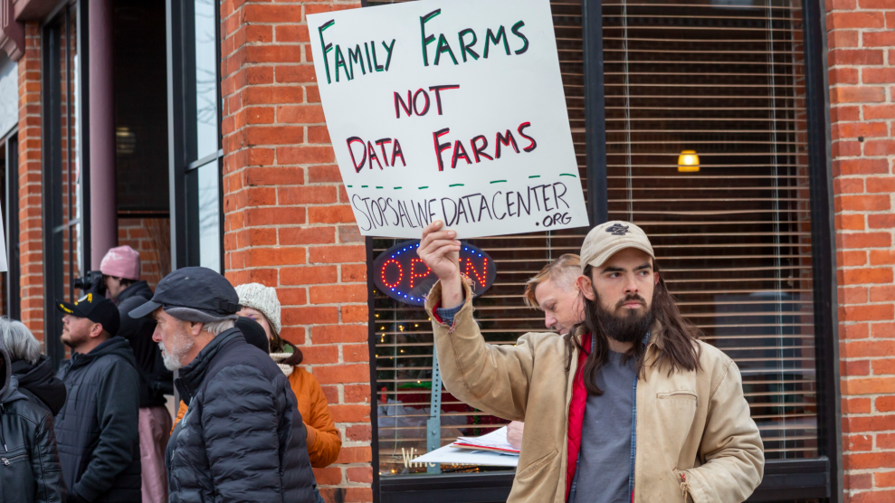 A person with long brown hair and a cropped brown beard holds a sign that says "family farms not data farms."
