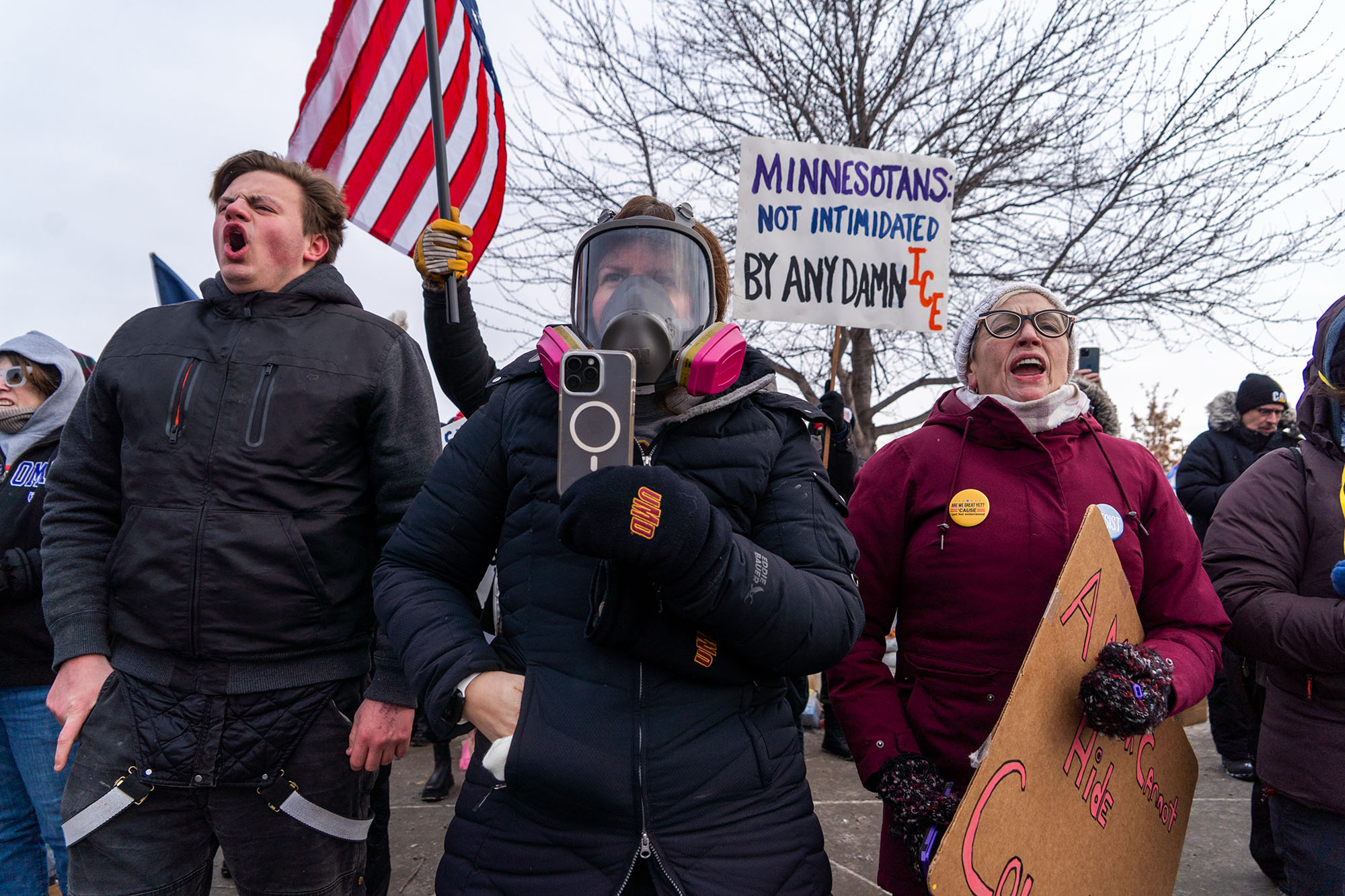 A group of protesters, one with a cellphone recording in the front of the crowd.